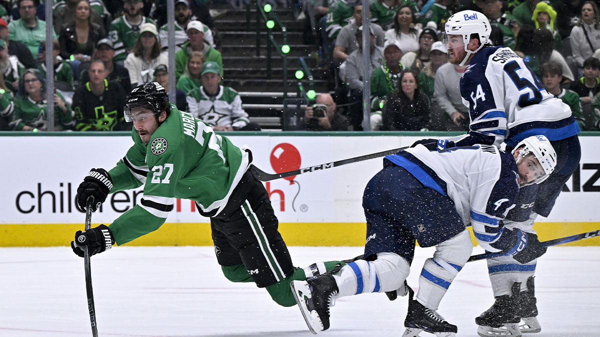 Dallas Stars left wing Mason Marchment (27) is tripped up as he shoots the puck past Winnipeg Jets defenseman Neal Pionk (4) and defenseman Dylan Samberg (54) during the second period in game three of the second round of the 2025 Stanley Cup Playoffs at American Airlines Center.